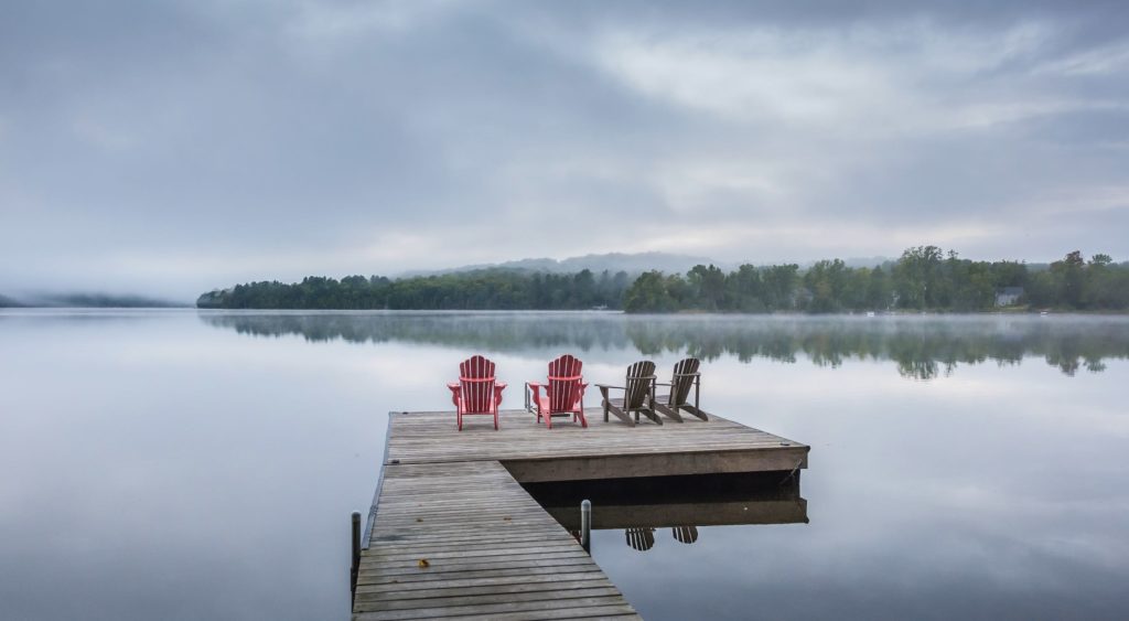 Dock and Muskoka chiars in Lake of Bays with morning mist over lake